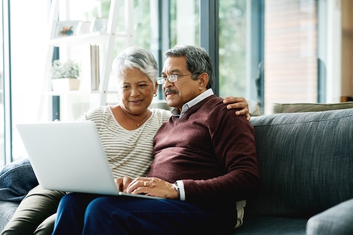 older coloured couple on the couch looking over the retirement plans with a laptop.