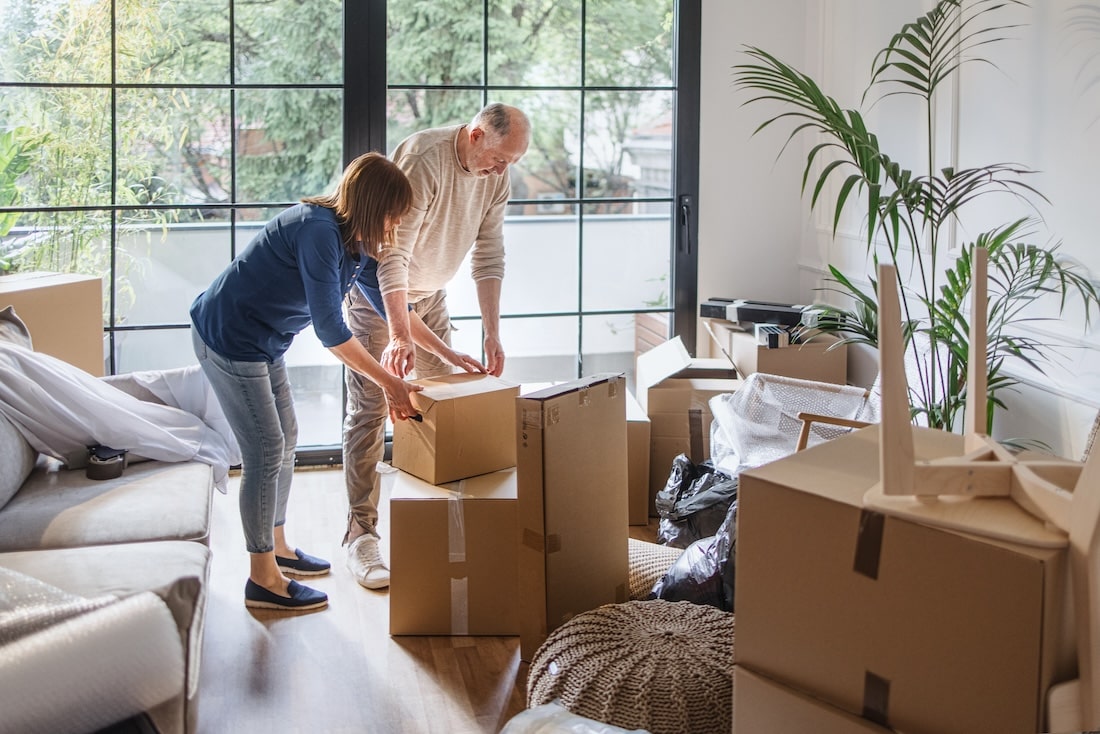 Elderly couple packing up boxes in front of a window of their living room.