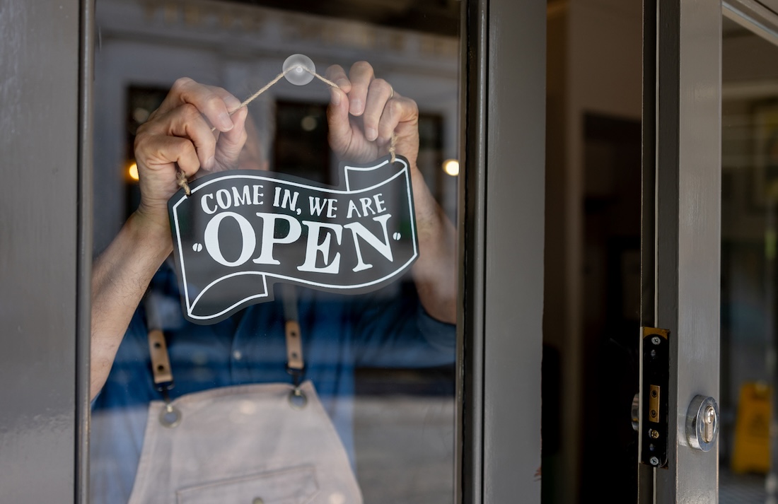 Close-up on a business owner hanging an open sign on the door of their restaurant.