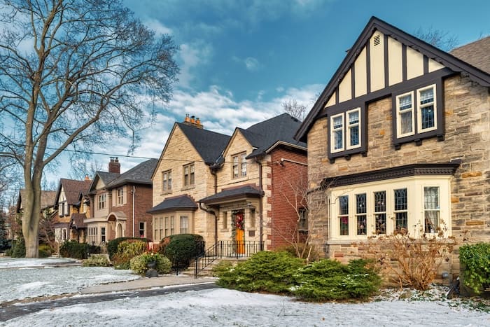 Neutral brown-coloured row houses in a residential neighbourhood with light snow on their front yards.