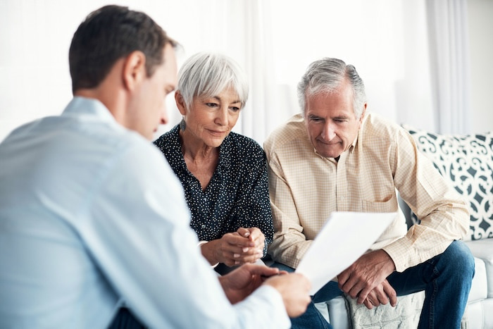 Consultant explaining real estate investment to an elderly couple on couches in their home.