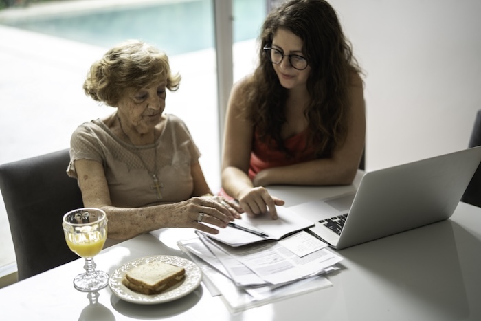 Younger woman with older family member going over papers outlining family generational wealth at a table with laptop and snacks.
