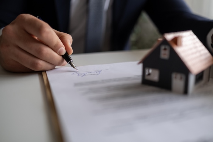 person signing documents with a miniature house on the table