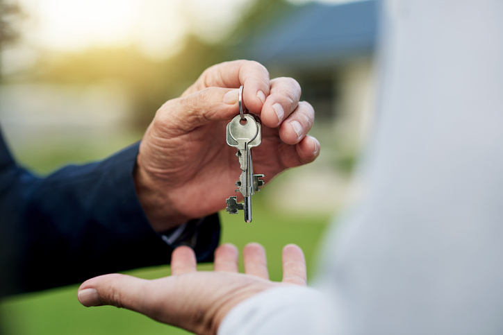 hands of elderly person giving keys to a house to another person.