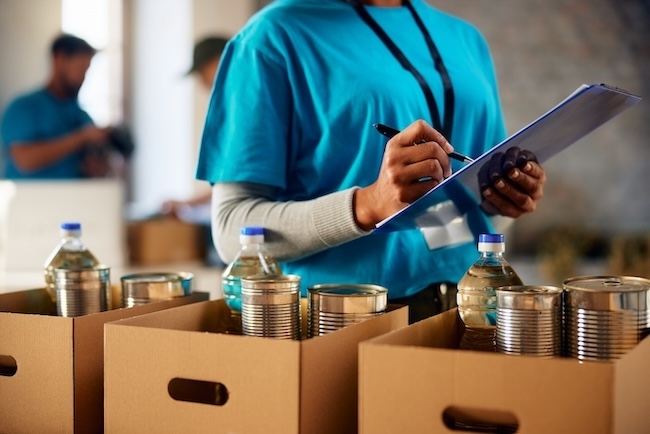 Close up of female volunteer making list of food supplies while working at humanitarian aid center.
