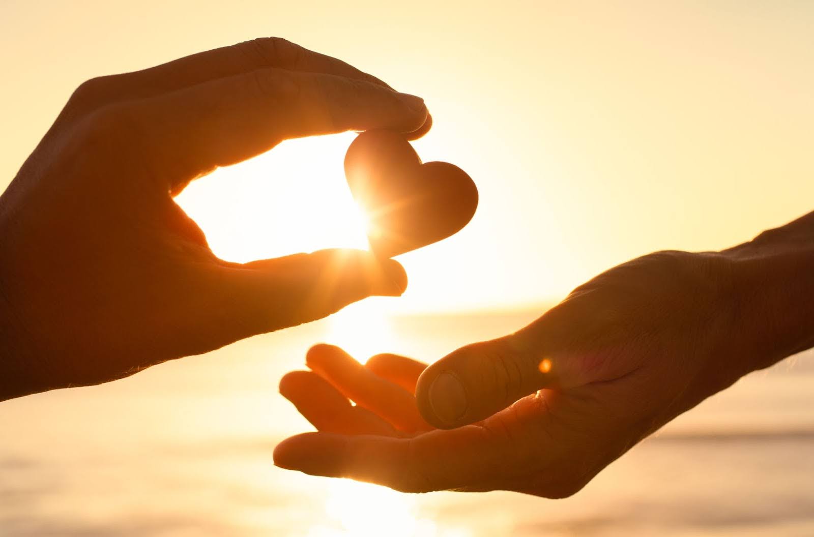 hands passing a heart in front of a sunset