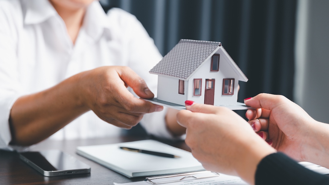 Two people's hands holding a home model, a small building to signify the great wealth transfer in Canada.